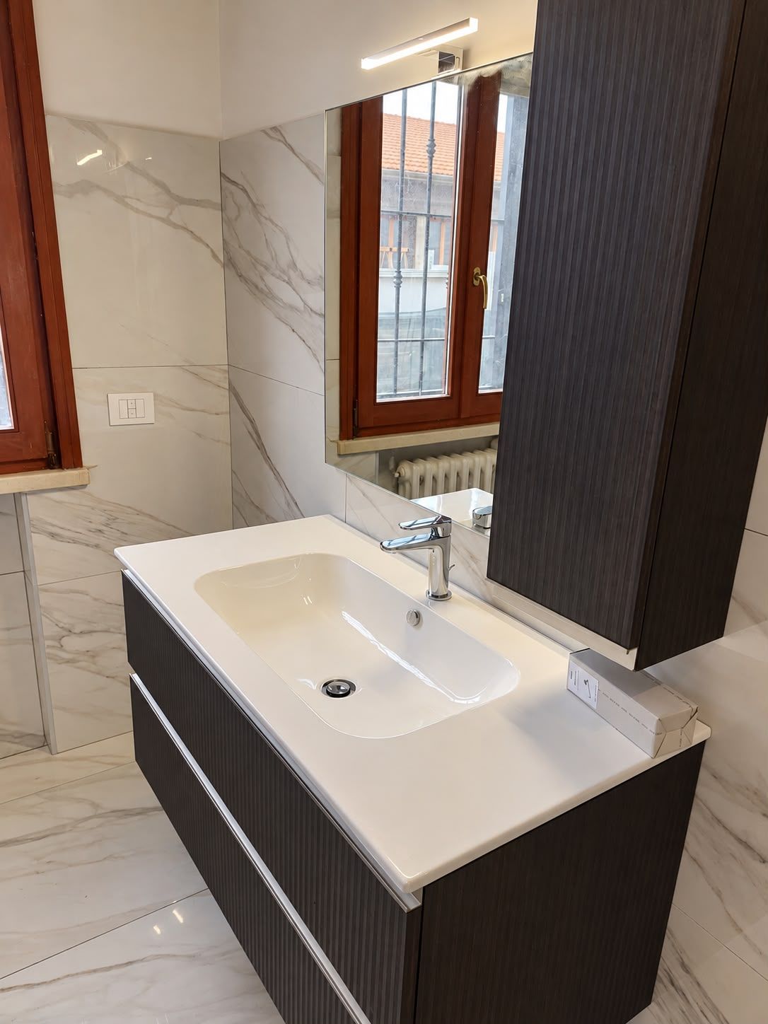 Mobile bagno con lavabo, specchio e rivestimento in marmo chiaro